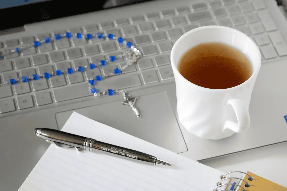 Web designer's laptop, tea, notebook, and rosary.